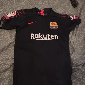 FC Barcelona målvaktströja Ter Stegen - Säljer en svart FC Barcelona målvaktströja med Ter Stegen och nummer 1 på ryggen. Tröjan har korta ärmar med röda ränder och klubbmärke på bröstet. Rakuten och UNICEF-loggor finns tryckta fram och bak. Tillverkad i lätt polyester, perfekt för match eller träning.