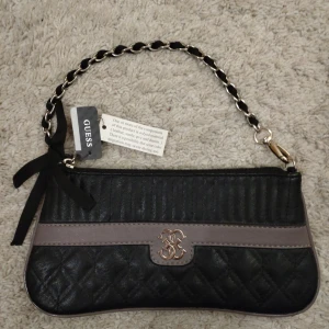 Helt ny äkta guess väska I läder - Helt ny, oanvänd äkta läder väska från guess. Äkthetsbevis på alla lapparna som fortfarande sitter på. Jättesöt väska med liten svart rosett på axelremmen. Kommer från ett pedantiskt djur och rökfritt hem