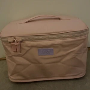 Rosa necessärväska från Lyko - Säljer en ljusrosa necessärväska från Lyko med praktiskt handtag upptill och dragkedja runt om. Väskan är rymlig och har en stilren, boxig form. Perfekt för att organisera smink eller hudvårdsgrejer när du är på språng. Helt nyköpt