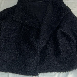 Blå teddyjacka - Mysig svart teddyjacka med stor, bred krage och boxig passform. Stängs med knapp framtill och har långa ärmar. Perfekt för kalla dagar när du vill vara både varm och snygg. Storlek S