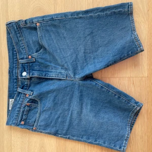 Levi's blå jeansshorts  - Säljer ett par klassiska blå jeansshorts från Levi's med hög midja och raka ben. Shortsen har fyra fickor, synliga nitar och dragkedja med knapp. Materialet är slitstarkt denim och passformen är normal. Perfekt för chill dagar och sommarhäng. Tveka inte med att slå ett pling, priset är ej hugget i sten.