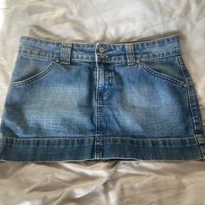 Blå jeanskjol från JAG - Säljer en snygg blå jeanskjol från JAG med  fickor fram och bak, dubbla knappar i midjan och bälteshällor. midjemått:41cm