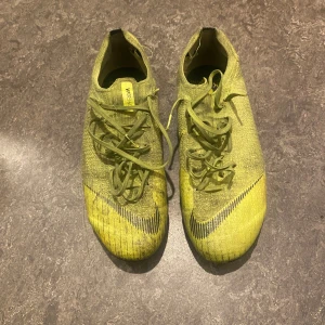 Nike Mercurial fotbollsskor - Säljer ett par Nike Mercurial fotbollsskor i en riktigt cool gul färg med svarta detaljer och snörning. Skorna har stickad ovandel och svarta dobbar för bästa grepp på planen. Perfekta för dig som vill sticka ut och ha maxad kontroll på bollen. Vissa dobbar är slitna, men fungerar fortfarande därmed det låga priset. Skick: 5/10