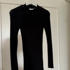 Svart ribbad klänning från Saint - Supersnygg svart ribbad tröja från Saint med lång ärm och volangdetalj vid ärmslut. Tight passform som framhäver figuren och hög hals. Perfekt för dig som gillar minimalistisk och stilren look. Aldrig använd. Storlek S men väldigt elastisk. Kan mötas på Ekerö annars skickar jag och köparen står för frakt 