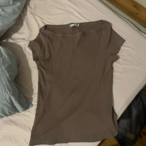 Brun ribbad topp från 157, storlek L - En basic brun ribbad topp från 157 i storlek L. Modellen är kortärmad med rund halsringning och har en slim passform. Perfekt att styla med jeans eller kjol för en enkel och clean look.