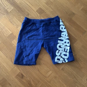 Blå shorts från Dsquared2 med tryck - Snygga blå shorts från Dsquared2 med stort vitt logotryck längs ena benet. Modellen har bekväm midja och två fickor framtill. Tillverkade i mjuk bomull, perfekta för sommardagar och chill outfits.