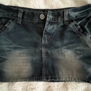 Mörk jeanskjol med slitningar - Snygg mörkblå jeanskjol med snygga detaljer och coola fickor både fram och bak. Kjolen har bälteshällor, knapp och dragkedja framtill samt röda sömdetaljer vid fickorna. Helt oanvänd.