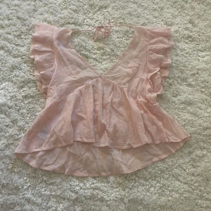 Rosa volangblus från Nelly - Supersöt ljusrosa blus från Nelly med volangärmar och v-ringning både fram och bak. Toppen har knytband i nacken och är tillverkad i ett tunt, luftigt bomullstyg. Perfekt för varma dagar när du vill känna dig extra fin💘