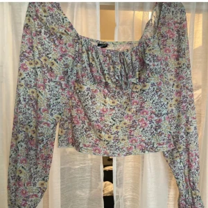 Blommig blus från Gina Tricot - Supersöt blommig blus från Gina Tricot i pastelliga toner av lila, rosa, gul och grön. Modellen har långärmade puffärmar, croppad passform och rynkade detaljer vid halsringningen. Perfekt för dig som gillar romantisk och trendig stil.