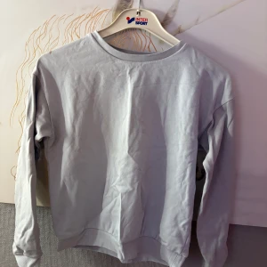 Ljusgrå sweatshirt från Kappahl - En basic ljusgrå sweatshirt från Kappahl i mjuk bomull. Tröjan har rund halsringning, ribbade muddar och lång ärm. Perfekt för en chill och enkel stil. Passar dig som gillar minimalistiskt och bekvämt. Finns lite fläck går nog bort i tvätten