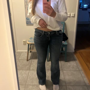 Blå bootcut jeans med broderade fickor - Säljer ett par snygga blå jeans med bootcut-modell och coola broderade detaljer på bakfickorna. Jeansen har låg midja och klassisk femficksdesign. Perfekta för dig som gillar en avslappnad men ändå trendig look.