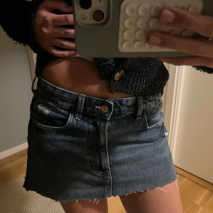 Mörkblå jeanskjol med rå kant - Säljer en snygg mörkblå jeanskjol med rå, fransig kant och slitna detaljer. Kjolen har klassiska fickor fram och bak samt bälteshällor. Perfekt för dig som gillar en avslappnad och trendig stil.