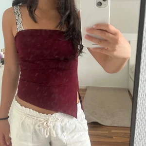 Vinröd asymmetrisk tubtopp - Säljer en vinröd tubtopp med cool asymmetrisk nederkant och liten slits på sidan. Toppen är bandeau-modell och har ett mjukt bomullsmaterial som sitter skönt mot kroppen. Perfekt för dig som gillar att sticka ut med enkla detaljer. Säljer då jag fick ingen användning av toppen! Mycket fint skick