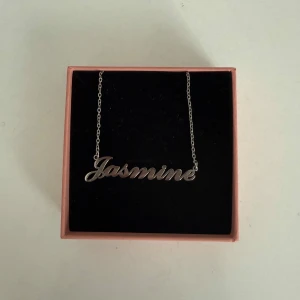 Silverplätterad halsband Jasmine - Stilrent silverplätterad halsband med namnet Jasmine i snygg skrivstil. Kedjan är tunn och elegant, perfekt för att ge en personlig touch till din look. Den har aldrig använts eftersom att jag är en guld tjej och fick den som present❤️