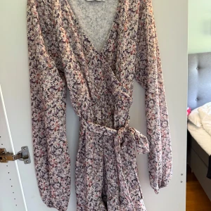 Blommig omlottklänning från Chiquelle - Supersöt kortklänning från Chiquelle i storlek XS med blommigt mönster i ljusa toner. Klänningen har omlottmodell med v-ringning, långa ärmar och ett knytband i midjan. Perfekt för dig som gillar romantisk och feminin stil. Klänningen är nu tyvärr för liten så där av att jag säljer den💕