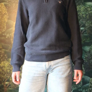 Mörkblå Gant half zip tröja - Säljer en mörkblå strukturerad tröja från Gant med halv dragkedja och broderad logga på bröstet. Tröjan har ribbade muddar och krage i kontrastfärg. Perfekt för dig som gillar klassisk och stilren look.