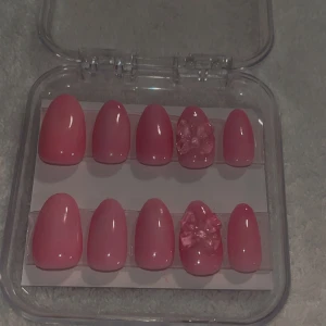 Pink jelly press ons size M - Säljer ett set med glansiga rosa lösnaglar i oval form. Två av naglarna har söta 3D-rosetter som detalj. Perfekt för dig som vill ha en söt och trendig look. Kommer i en praktisk förvaringsask.