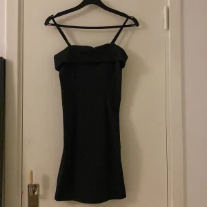 Svart kort klänning med smala axelband - Snygg svart klänning med smala axelband och en bred, vikt kant upptill. Modellen är kort och har en stilren, rak passform som ger en chic vibe. Perfekt för dig som gillar minimalistisk stil och vill ha en enkel men elegant look.