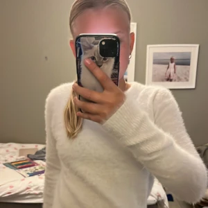 Vit fluffig stickad tröja från Zara - Supermjuk och fluffig vit stickad tröja från Zara med rund hals och långa ärmar. Tröjan har ribbade muddar vid ärmslut och nederkant, vilket ger en snygg och enkel look. Perfekt för dig som gillar en clean och cozy stil.