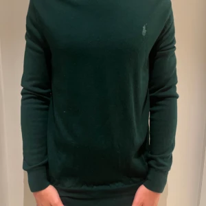 Mörkgrön stickad tröja från Ralph Lauren - Mörkgrön stickad tröja från Ralph Lauren med diskret broderad logga på bröstet. Klassisk rund halsringning och långa ärmar. Tröjan har en normal passform och är perfekt för dig som gillar stilren och enkel design. Otroligt bra skick knappt använd. Modellen är 187 och väger 75