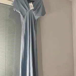 Ljusblå satin klänning från Zara  med v-ringning - Blå satin klänning från Zara storlek S, har aldrig använts och har prislappen kvar, köpt nyligen så den är helt ny