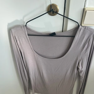 Ljusbeige långärmad topp Gina Tricot - En stilren ljusbeige långärmad topp från Gina Tricot med rundad, djup urringning. Tunn och mjuk i materialet, perfekt att styla med jeans eller kjol. Enkel och clean look som funkar till många outfits.