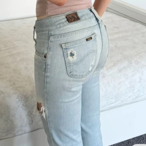 Ljusblåa lågmidjade bootcut jeans med slitningar  - Midja: ca 38 cm + mycket stretch! Innerben: ca 86 cm💕Första bild lånad! Lite trasig på ena fickan men inget man tänker på, se sista bild! Finns även 3 pyttesmå fläckar som knappt märks, skriv för bild på dessa💕 