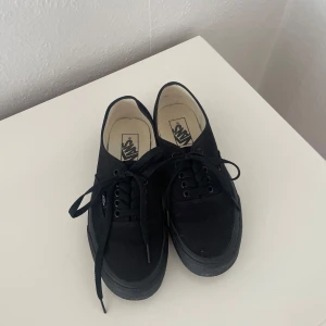 Svarta Vans sneakers - Klassiska svarta Vans sneakers med snörning och diskret Vans-logga på sidan samt röd logga bak på hälen.