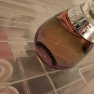 Parfymflaska Este lauder vintage - Säljer en snygg parfymflaska från este lauder. Flaskan är droppformad med en övergång från lila till bärnstensfärgad och har ett silvrigt metallband runt halsen. Spraykorken är transparent och rundad. Perfekt för dig som gillar lyxiga dofter och snygg design.