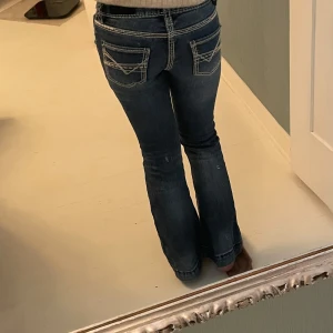 Rock & Roll Denim blå bootcut jeans girl - Snygga blå jeans från Rock & Roll Denim med kontrastsömmar och coola bakfickor med broderade detaljer. Modellen är bootcut med låg midja och klassisk femficksdesign. Perfekta för dig som gillar en avslappnad men trendig look.