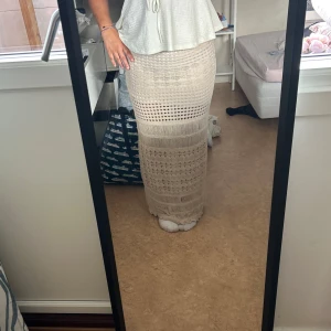 Beige långkjol i virkad stil - Säljer en beige långkjol med virkad look och olika mönstrade sektioner. Kjolen är figurnära och har transparenta partier som ger en cool boho-vibe. Perfekt för dig som gillar unika detaljer och vill sticka ut lite extra.