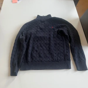 Mörkblå stickad tröja med dragkedja från Polo Ralph Lauren - Passar storlek S. Säljer en mörkblå stickad tröja från Polo Ralph Lauren med halv dragkedja och hög krage. Tröjan har kabelstickat mönster och en liten röd logga på bröstet. Insidan av kragen har röda och blå ränder för en snygg detalj. Använd väldigt få gånger, mycket fint skick. Nypris 1600kr