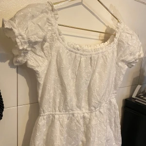 Vit blommig klänning med puffärm - Söt vit klänning med broderade blommor och puffiga korta ärmar. Klänningen har resår vid halsringningen och midjan för en bekväm passform. Perfekt för sommarens alla tillfällen!