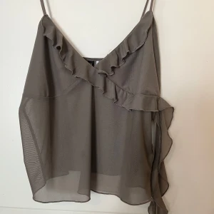 Ärmlös linne  - Fint grått linne med volanger. Perfekt för sommaren. lite y2k stil. Genomskinlig i magen och ryggen men täcker bysten. 
