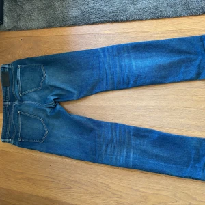 Blå jeans från BOSS - Säljer ett par klassiska blå jeans från BOSS med rak/slim passform. Jeansen har fem fickor och normal passform, perfekt för en stilren vardagslook. Tidlös design med läderpatch bak i midjan. 33/32