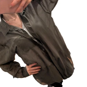Transparent kaki skjorta - Säljer en oversized transparent grå skjorta med klassisk krage och knäppning framtill. Skjortan har långa ärmar och är tillverkad i ett tunt, syntetmaterial som ger en luftig känsla. Perfekt att styla lager på lager eller över ett linne.