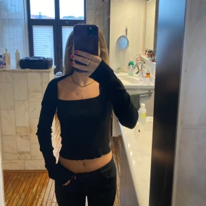 Svart croppad långärmad topp - Säljer en svart, ribbad och croppad långärmad topp med fyrkantig ringning. Toppen har en tight passform och är perfekt att styla med höga jeans eller kjol. Enkel och stilren design som passar till många olika looks.