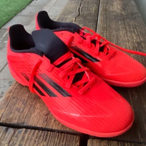 Röda fotbollsskor från Adidas - Säljer ett par röda Adidas fotbollsskor med svarta detaljer och snörning. Skorna har en sportig design med låg profil och svarta ränder på sidorna. Perfekta för dig som vill sticka ut på planen.