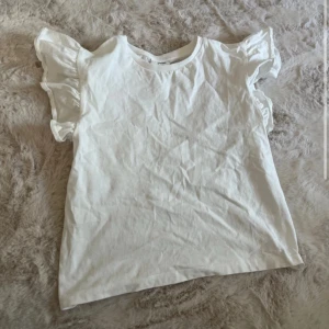 Vit volangtopp från Kappahl - Säljer en söt vit topp från Kappahl med volangdetaljer på ärmarna. Toppen har rund halsringning och är tillverkad i bomull!🩶