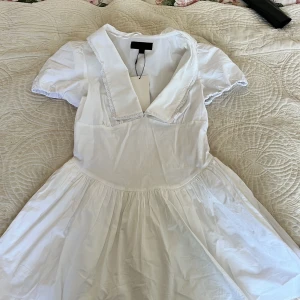 Vit kortklänning med krage från ZARA - Supersöt vit klänning från ZARA med korta puffärmar och bred krage med spetskant. Klänningen har en utställd kjol och är tillverkad i bomull, perfekt för sommarens alla tillfällen. Klassisk och fräsch look!