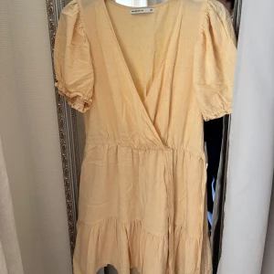 Ljusgul omlottklänning med puffärm - Söt ljusgul klänning i linnemix med omlottliv och puffiga korta ärmar. Klänningen har volang nertill och en luftig passform, perfekt för varma dagar. Tillverkad i ett lätt material som känns skönt mot huden.