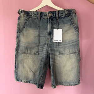 Blå jeansshorts från Bershka - Säljer ett par blå jeansshorts från Bershka med normal passform. Shortsen har stora fickor både fram och bak samt hällor för bälte. Perfekta för sommaren och har en cool, tvättad look. Oanvända!