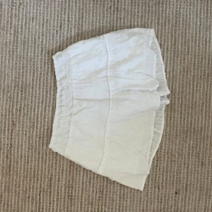 Vit kortkjol med volang - Säljer en söt vit kortkjol med volangdetalj och resår i midjan. Kjolen är luftig och perfekt för varma dagar. Passar till många olika stilar och är enkel att matcha med olika toppar.