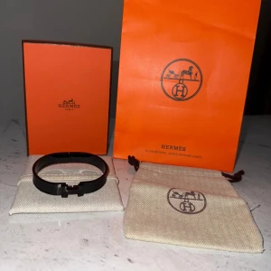 H3rmes armband  - Säljer ett stilrent svart armband med klassisk H-detalj framtill. Armbandet är i metall och levereras med originalpåse och ask. Perfekt accessoar för att lyfta din outfit.