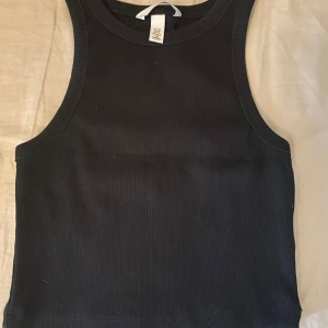 Grå ribbad croppad t-shirt - Grå croppad t-shirt med ribbad struktur och korta ärmar. Perfekt för en avslappnad och stilren look. Enkel att matcha med jeans eller kjol. Samt ett svart linne. Båda kan köpas för 70kr 