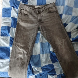 Grå jeans från Stock & Hank - Säljer ett par grå jeans från Stock & Hank med klassisk femficksdesign och dragkedja. Jeansen har normal passform och raka ben, perfekta för en avslappnad stil. Materialet är denim och färgen är en snygg tvättad grå.
