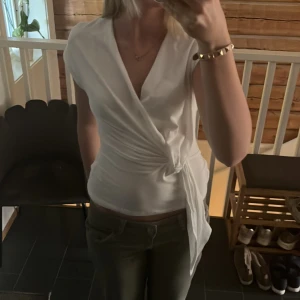 Vit omlottopp från SHEIN Strl S - Säljer en vit omlottopp från SHEIN med knyt i midjan och korta ärmar. Toppen har en v-ringad design och är tillverkad i ett mjukt, syntetiskt material. Perfekt för en stilren och fräsch look.