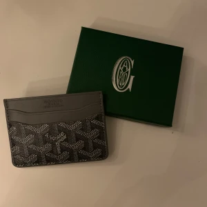 Grå korthållare  - Säljer en stilren grå korthållare med klassiskt mönster och logga framtill. Korthållaren har flera fack för kort och är perfekt för dig som vill ha något både snyggt och praktiskt i fickan. Kommer med originalask.