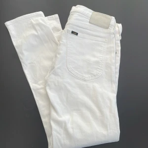 Vita jeans från Lee - Säljer ett par klassiska vita jeans från Lee med fem fickor och silverfärgade nitar. Byxorna har normal passform och raka ben. Perfekta för en stilren look och lätta att matcha med olika outfits.