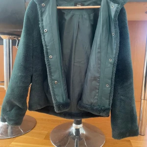 Mörkgrön pälsjacka från ONLY - Säljer en mörkgrön pälsjacka från ONLY med lång ärm och mjuk, fluffig känsla. Jackan har dold knäppning framtill och två fickor på sidorna. Perfekt för dig som vill ha en stilren och mysig jacka till kyligare dagar. Skulle säga att den är liten i storleken o mer passar M